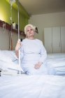 Задумчивая пожилая женщина, сидящая на кровати в больнице — стоковое фото