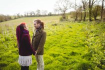 Пара хипстеров держится за руки, стоя на травянистом поле в парке — стоковое фото