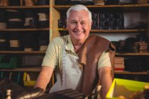 Портрет улыбающегося сапожника, сидящего в мастерской — стоковое фото