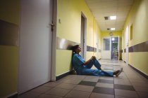 Depressed nurse sitting in hospital corridor — Stock Photo