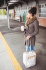 Woman holding disposable coffee cup while standing at railway station platform — Stock Photo