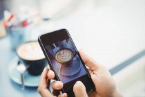 Руки держат мобильный телефон с фотографией кофе в ресторане — стоковое фото