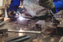 Immagine ritagliata del saldatore maschio che lavora su pezzo di metallo in officina — Foto stock