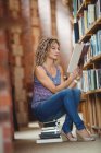 Mujer sentada y leyendo libro en la biblioteca - foto de stock