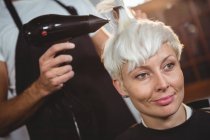 Усміхнена жінка висушує волосся в перукарні — стокове фото