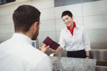 Atendente de check-in da companhia aérea que entrega passaporte ao passageiro no balcão de check-in do aeroporto — Fotografia de Stock