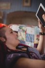 Donna hipster che utilizza tablet digitale mentre si rilassa sul divano di casa — Foto stock