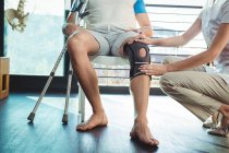 Immagine ritagliata del fisioterapista femminile che esamina il ginocchio del paziente in clinica — Foto stock