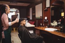 Жіночий перукар показує чоловікові свою зачіску в дзеркалі в перукарні — стокове фото