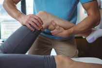 Обрезанное изображение мужского физиотерапевта, делающего массаж колен пациентке в клинике — стоковое фото