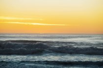 Puesta de sol sobre las olas en la playa - foto de stock