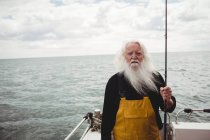 Retrato de pescador em pé no barco segurando haste de pesca — Fotografia de Stock
