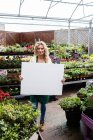 Portrait of smiling female florist holding blank placard in garden centre — Stock Photo