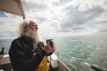 Pescador de cabelo cinza pensativo em pé no barco com xícara de café — Fotografia de Stock