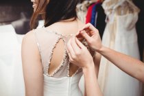 Imagen recortada de la mujer que intenta en el vestido de novia en el estudio con la ayuda del diseñador creativo - foto de stock