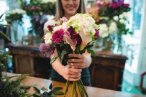 Imagem cortada de florista feminina segurando monte de flores em sua loja de flores — Fotografia de Stock