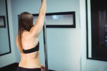 Rückansicht der Pole-Tänzerin, die im Fitnessstudio die Stange hält — Stockfoto
