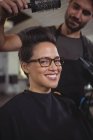 Портрет усміхненої жінки, яка сушить волосся феном у перукарні — стокове фото