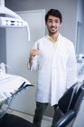 Retrato de dentista sorridente em pé com ferramentas odontológicas na clínica odontológica — Fotografia de Stock