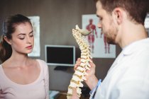 Fisioterapeuta explicando columna vertebral a paciente femenina en clínica - foto de stock