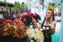 Floristin telefoniert mit Handy, während sie Blumen im Blumenladen arrangiert — Stockfoto