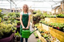 Portrait of female florist holding watering can in garden centre — Stock Photo