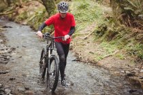 Front view of male biker walking with bicycle in stream at forest — Stock Photo