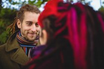 Sorrindo hipster olhando para a mulher enquanto estava em pé no parque — Fotografia de Stock