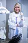 Portrait of smiling dentist holding dental tools at dental clinic — Stock Photo