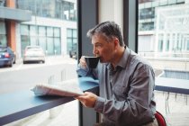 Man holding newspaper and having coffee in cafeteria — Stock Photo