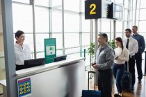 Пассажиры, стоящие в очереди у стойки регистрации в терминале аэропорта — стоковое фото