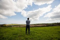 Vue arrière de l'homme debout sur un champ herbeux contre un ciel nuageux — Photo de stock