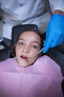 Dentista examinando paciente joven con herramientas en clínica dental - foto de stock