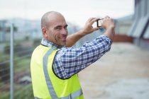 Construction worker photographing with mobile phone outside office — Stock Photo
