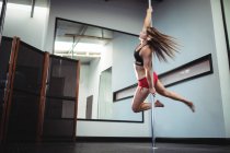 Baixo ângulo de visão da bela dançarina Pole praticando pole dance no estúdio de fitness — Fotografia de Stock