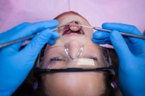 Dentista examinando paciente joven con herramientas en clínica dental - foto de stock