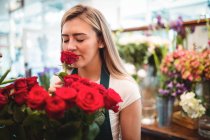Fiorista donna che annusa un fiore di rosa nel negozio di fiori — Foto stock