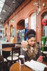 Жінка використовує телефон, сидячи в ресторані на залізничній станції — стокове фото
