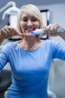 Улыбающаяся женщина надевает зубную пасту на щетку в стоматологической клинике — стоковое фото