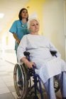 Медсестра штовхає старшого пацієнта на інвалідне крісло в лікарні — стокове фото