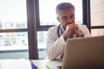 Portrait of doctor with stethoscope sitting at desk at hospital — Stock Photo