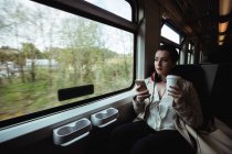Young woman using mobile phone by window in train — Stock Photo
