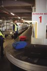 Tripulação de terra do aeroporto descarregando bagagem do carrossel de bagagem no terminal do aeroporto — Fotografia de Stock