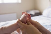 Cropped image of mother holding baby feet on bed at home — Stock Photo