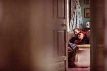 Couple hipster romantique assis sur un canapé vu de la porte à la maison — Photo de stock