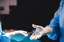 Hands of surgeon giving operation scissors to colleague in operation room at hospital — Stock Photo