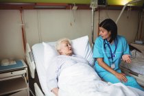 Enfermera interactuando con paciente mayor en el hospital - foto de stock