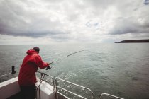 Vista trasera de la pesca del pescador con caña de pescar del barco - foto de stock