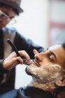 Homem com barba raspada com navalha na barbearia — Fotografia de Stock