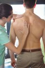 Fisioterapeuta femenina dando masaje de espalda a paciente masculino en clínica - foto de stock